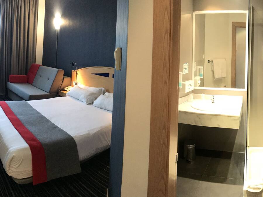 Una habitación de hotel con cama, sofá, escritorio y baño con lavamanos y espejo.