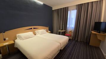 A hotel room with two beds, a TV, a desk, and a chair.
