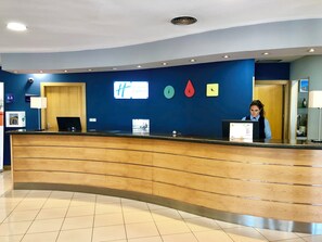 A hotel reception desk with a blue wall, a clock, and a sign for 'Hampton Inn Express'. - Holiday Inn Express Madrid-San Sebastian de los Reyes by IHG (San Sebastian de los Reyes)