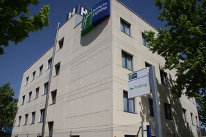 A multi-story building with a Holiday Inn Express sign, a parking sign, and a chain-link fence. - Holiday Inn Express Madrid-San Sebastian de los Reyes by IHG (San Sebastian de los Reyes)