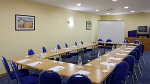 Une salle de conférence avec de longues tables, des chaises, des bouteilles d’eau et un tableau blanc.