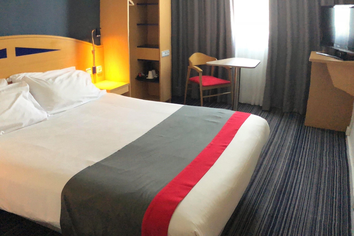 Hotellihuone, jossa on sänky, työpöytä, tuoli, televisio ja vaatekaappi.
