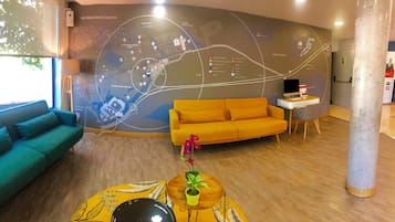 Un interior moderno con un gran mapa mural, un sofá verde azulado, un sofá amarillo, una mesita con una planta y un escritorio con una computadora.