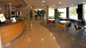 Un espace intérieur vaste et lumineux, comprenant un comptoir d’accueil, plusieurs coins salon et de grandes fenêtres qui laissent entrer la lumière naturelle.