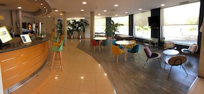 A spacious indoor area with a reception desk, multiple seating arrangements, and large windows providing natural light.