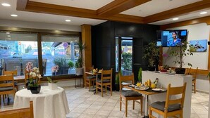 Um saguão de hotel com cadeiras e mesas de madeira, um balcão de recepção e uma tela de televisão.