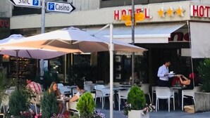 Uma área externa com mesas e guarda-sóis, uma placa de hotel e sinalização indicativa para SMC e Casino.