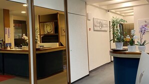 Uma área de recepção com balcão, painéis de madeira e plantas em vasos.