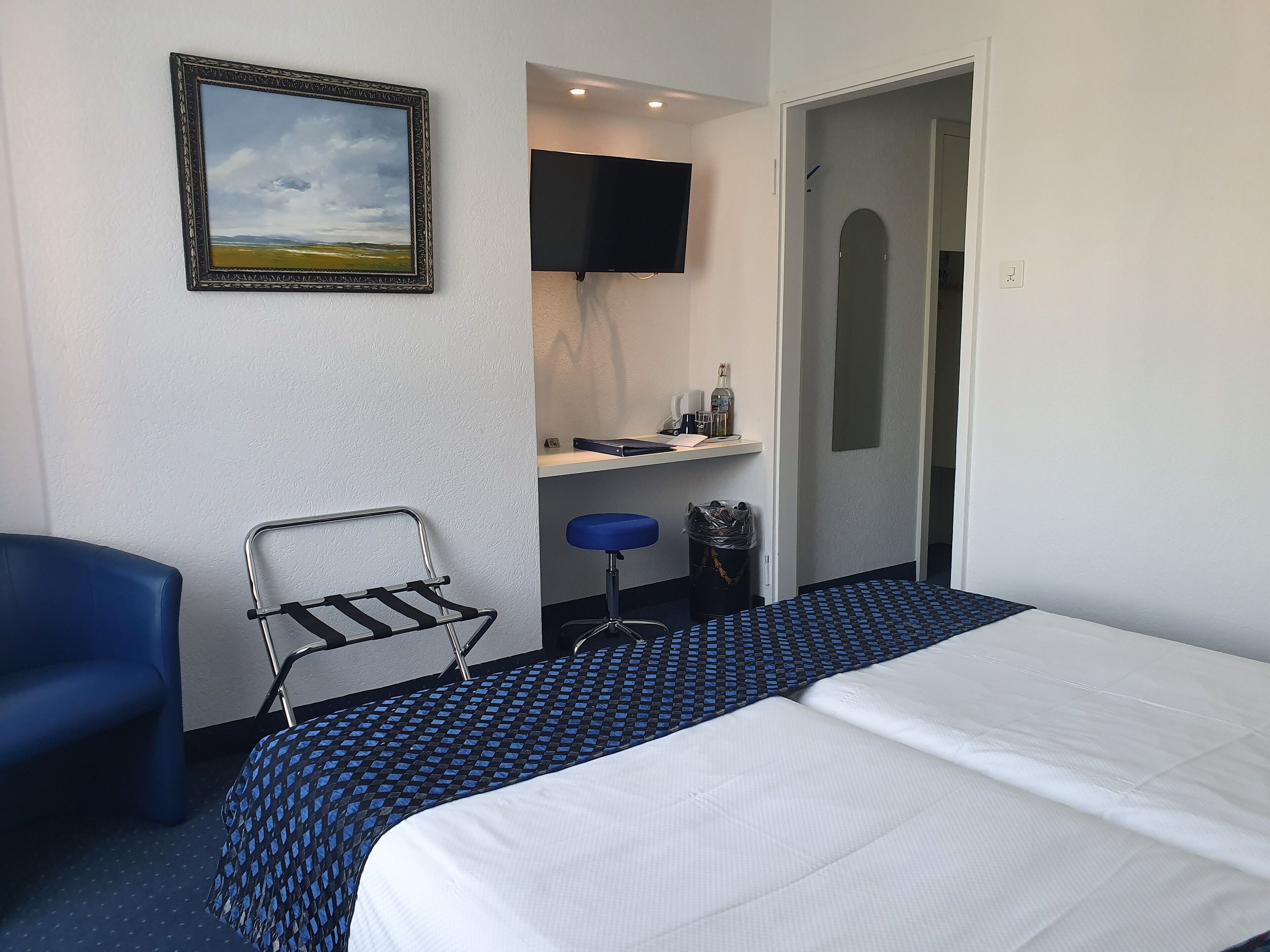 Een hotelkamer met een bed, een stoel, een televisie, een klein bureau en een foto aan de muur.