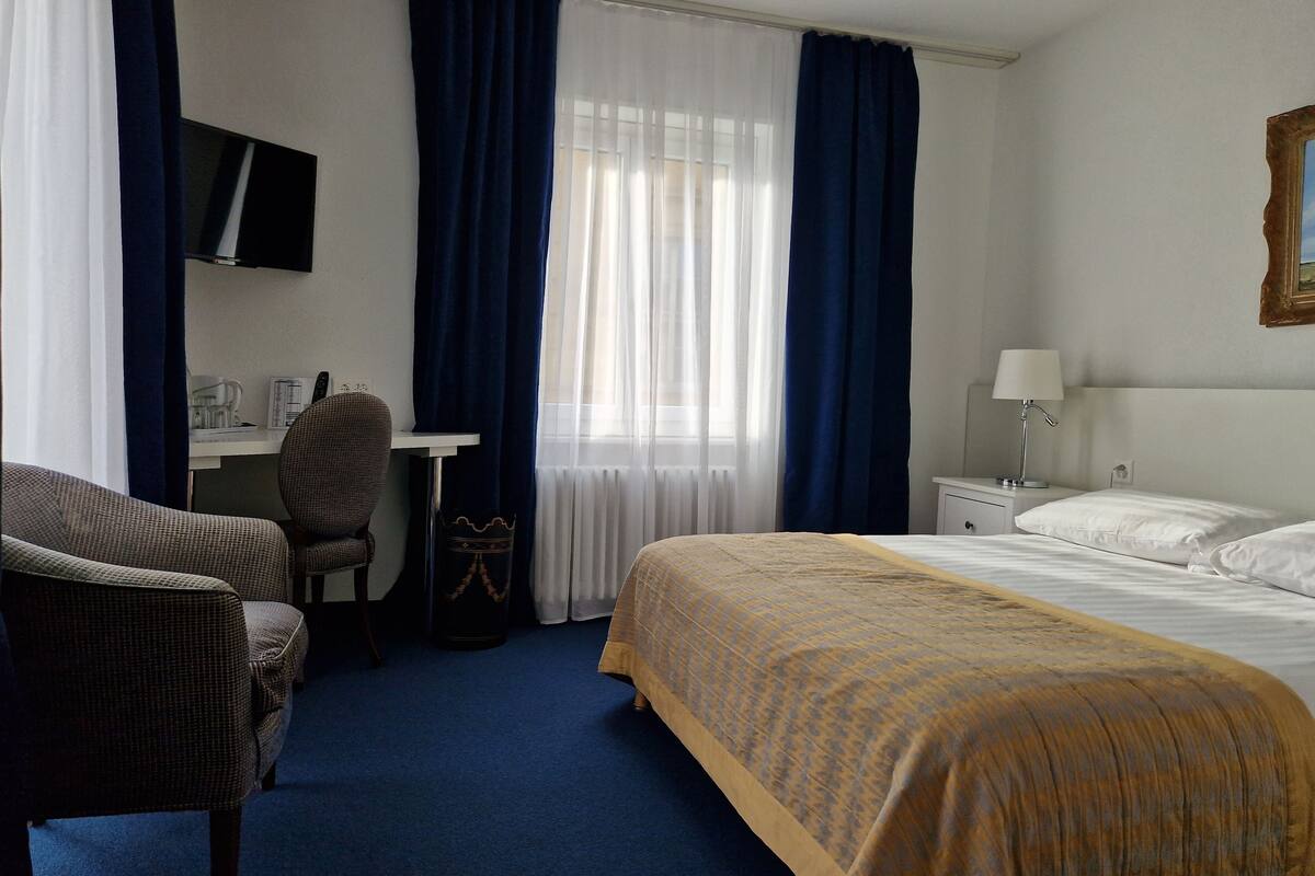 A hotel room with a bed, a desk, a chair, a TV, and a window with curtains.