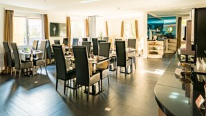 Un comedor amplio de hotel con múltiples mesas y sillas, una zona de cocina y una barra.
