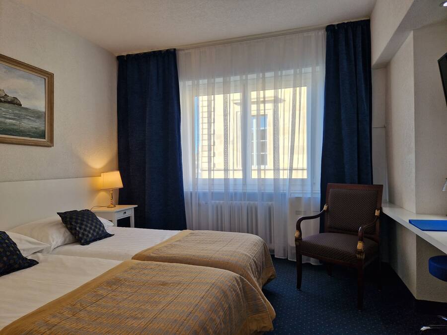 Habitación de hotel con dos camas, un escritorio, una silla, una lámpara y una ventana con cortinas.