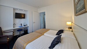 Habitación de hotel con dos camas, un escritorio con televisor de pantalla plana, una silla y una mesita de noche con lámpara.