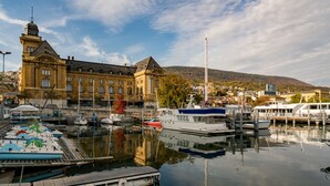Un puerto deportivo con barcos amarrados, un edificio grande con una torre y una colina al fondo.