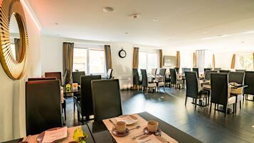 A hotel dining area with multiple tables and chairs, a large mirror, and a clock on the wall.