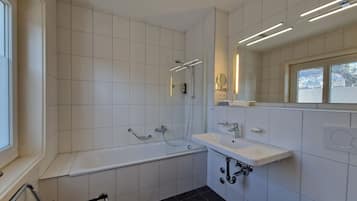 A modern bathroom with white tiles, a bathtub, a sink, and a toilet.