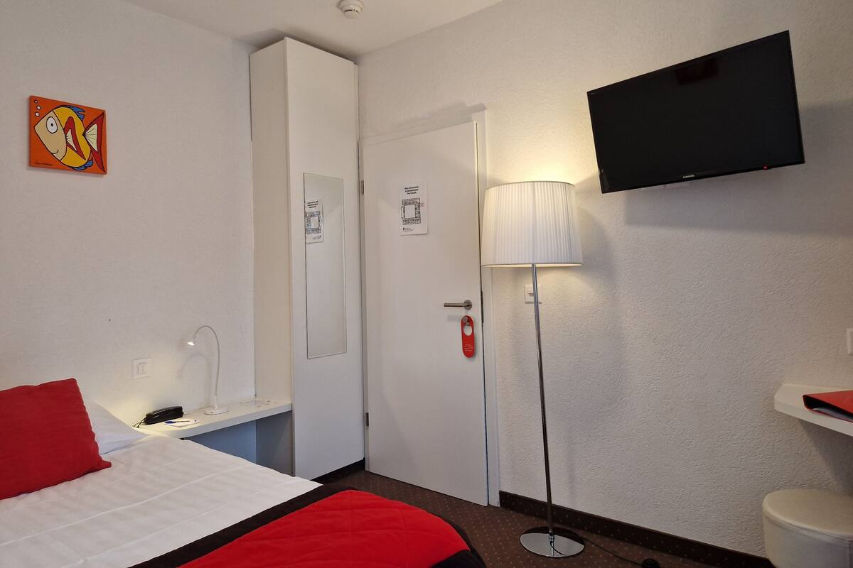 A hotel room with a bed, a desk, a telephone, a television, and a lamp.