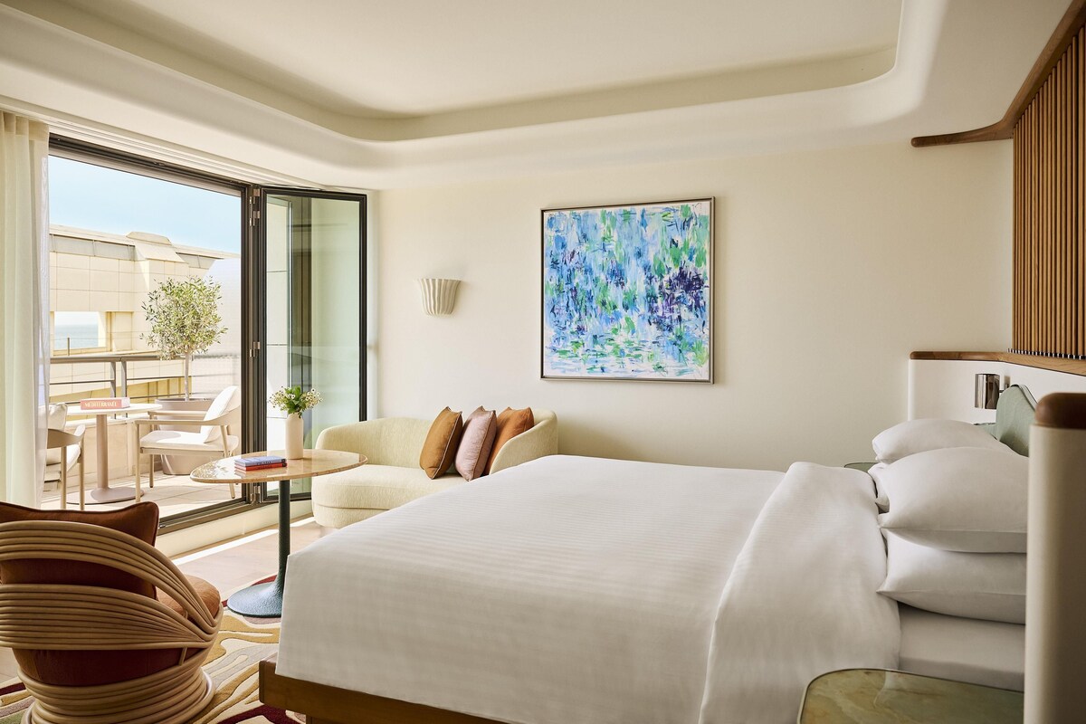 A hotel room with a large bed, a sofa, a small table, and a view of the outside.