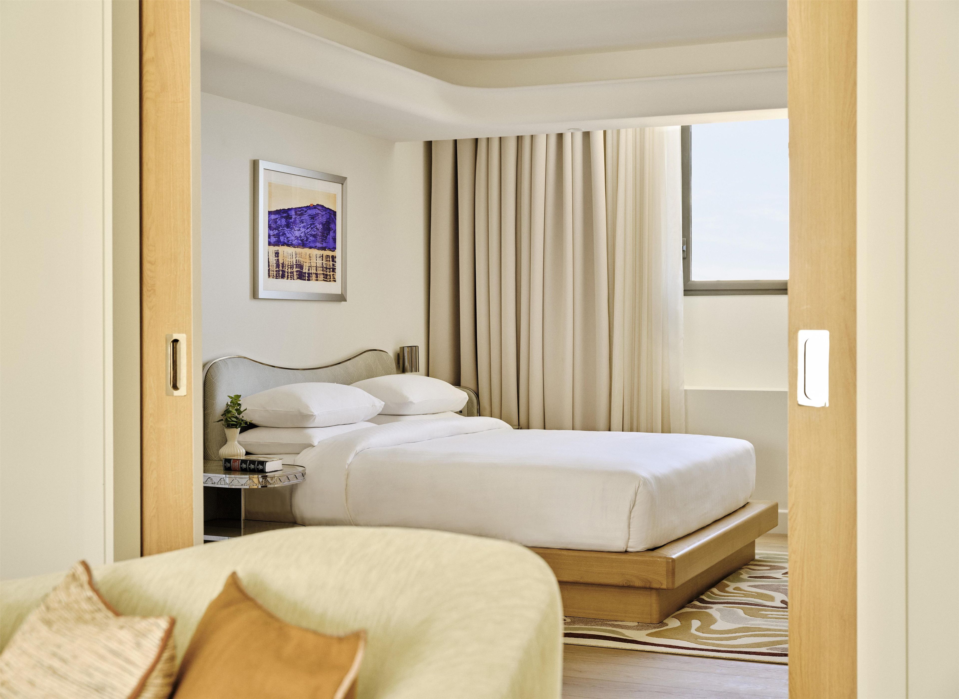 Una habitación de hotel con cama, mesita de noche, lámpara y un cuadro en la pared.