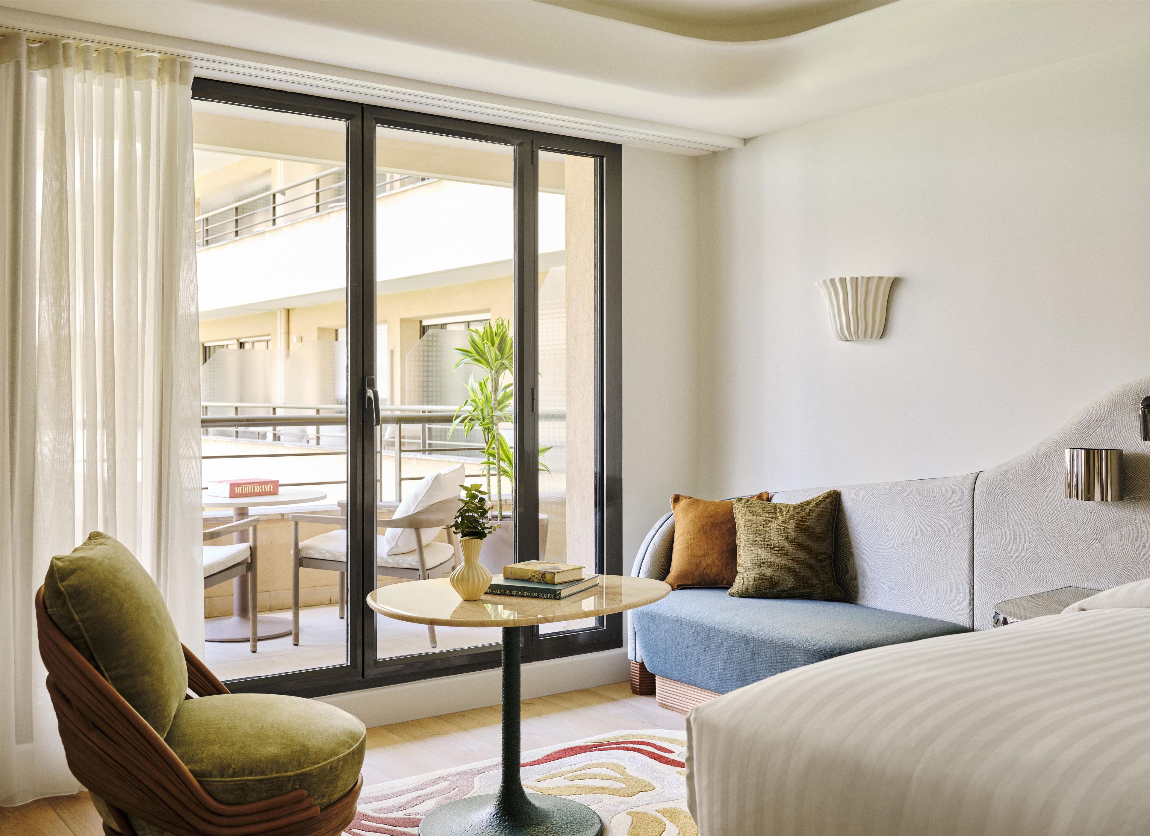 A hotel room with a balcony, a sofa, a chair, a small round table, and a bed.
