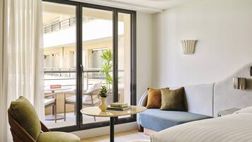 A hotel room with a balcony, a sofa, a chair, a small round table, and a bed.