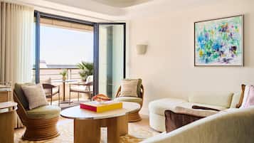 A modern living room with a round coffee table, two armchairs, a sofa, a dining table with chairs, a large window, and a colorful abstract painting on the wall.