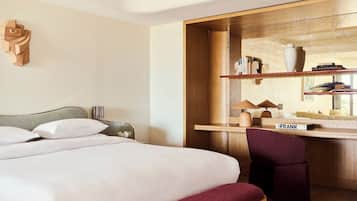 A hotel room with a bed, a desk, a chair, and a bookshelf.