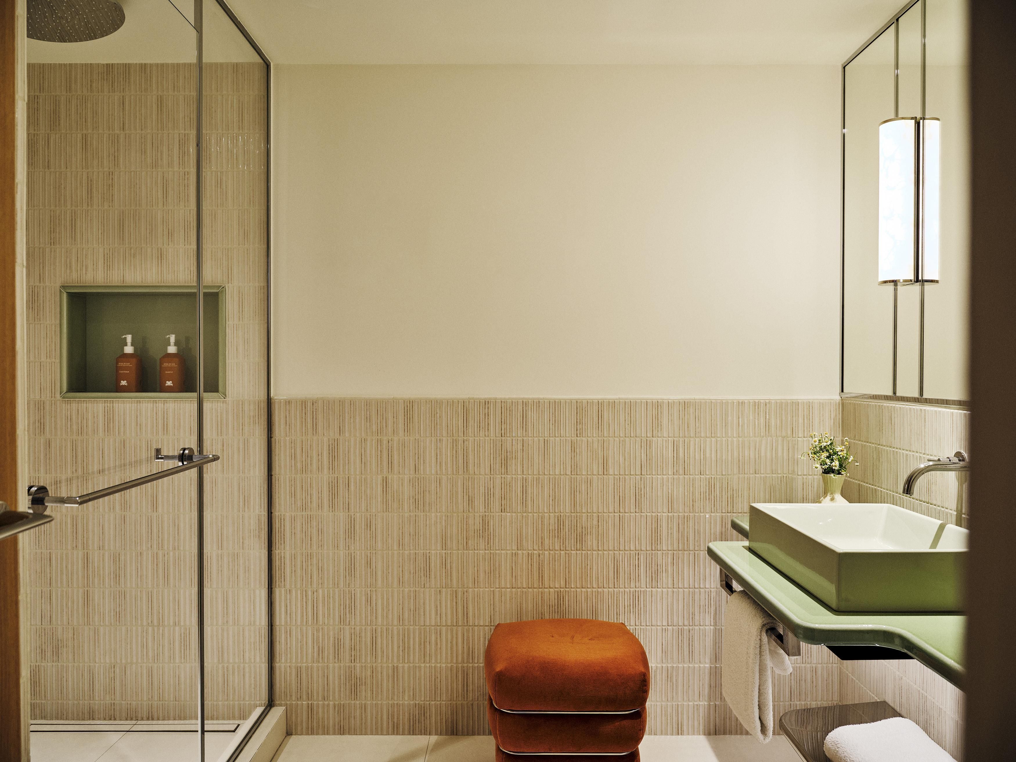 A modern bathroom with a glass shower enclosure, a green sink vanity, and a small shelf with toiletries.