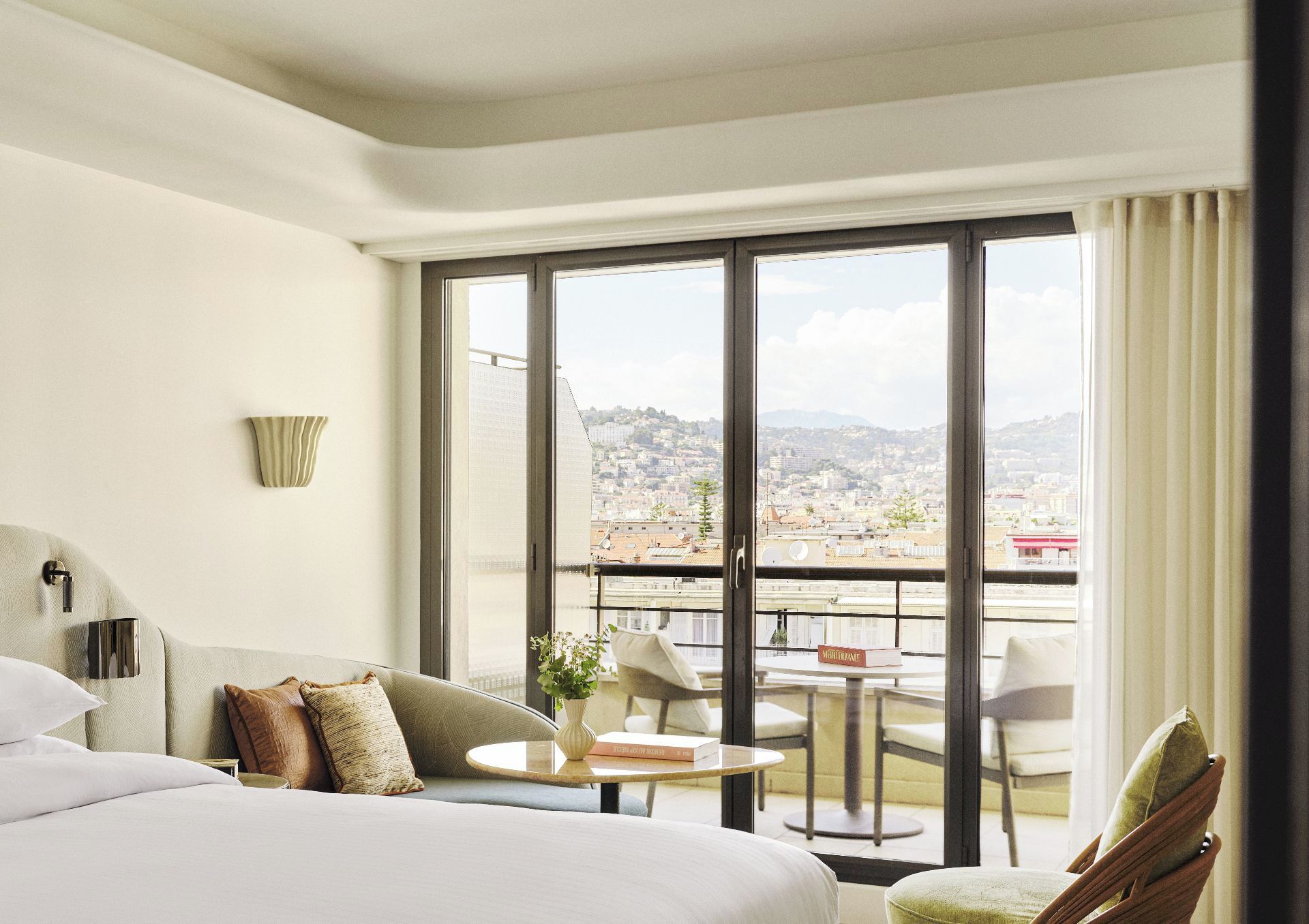 Une chambre d’hôtel dotée d’un grand lit, d’un coin salon avec une table et des chaises, et d’un balcon offrant une vue sur la ville.