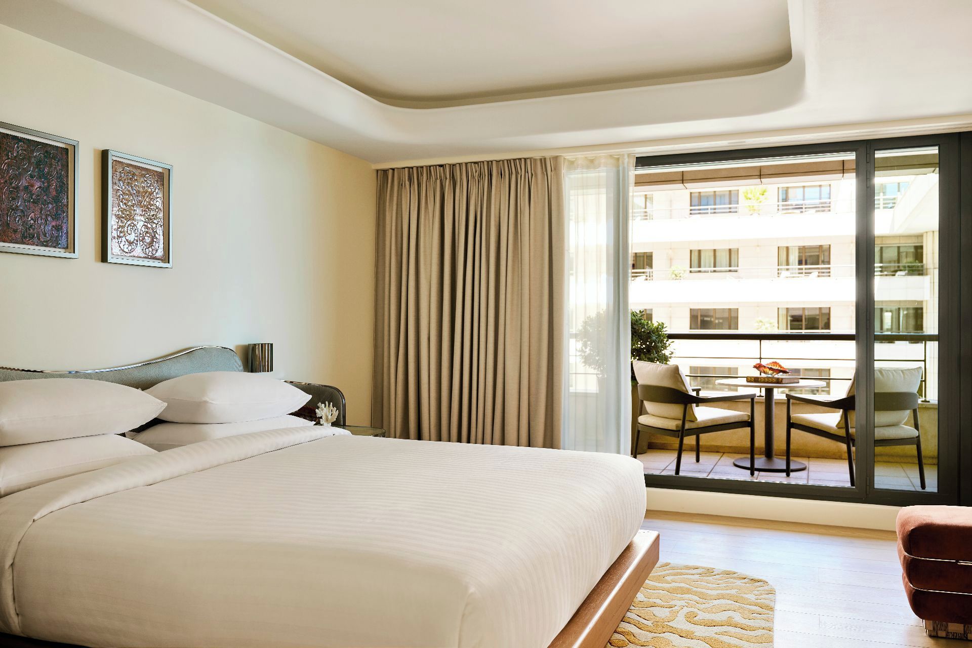 Een hotelkamer met een bed, een klein tafeltje, een stoel en een balkon met uitzicht op het gebouw.