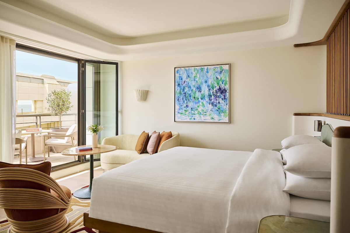 A hotel room with a large bed, a sofa, a small table, and a view of the outside.