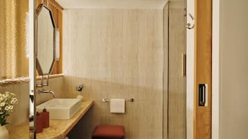 Un baño moderno con cabina de ducha de vidrio, encimera de mármol y mueble de tocador de madera.