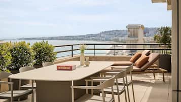 Una terraza con una mesa, sillas, un sillón de descanso y vistas a la ciudad y al agua.