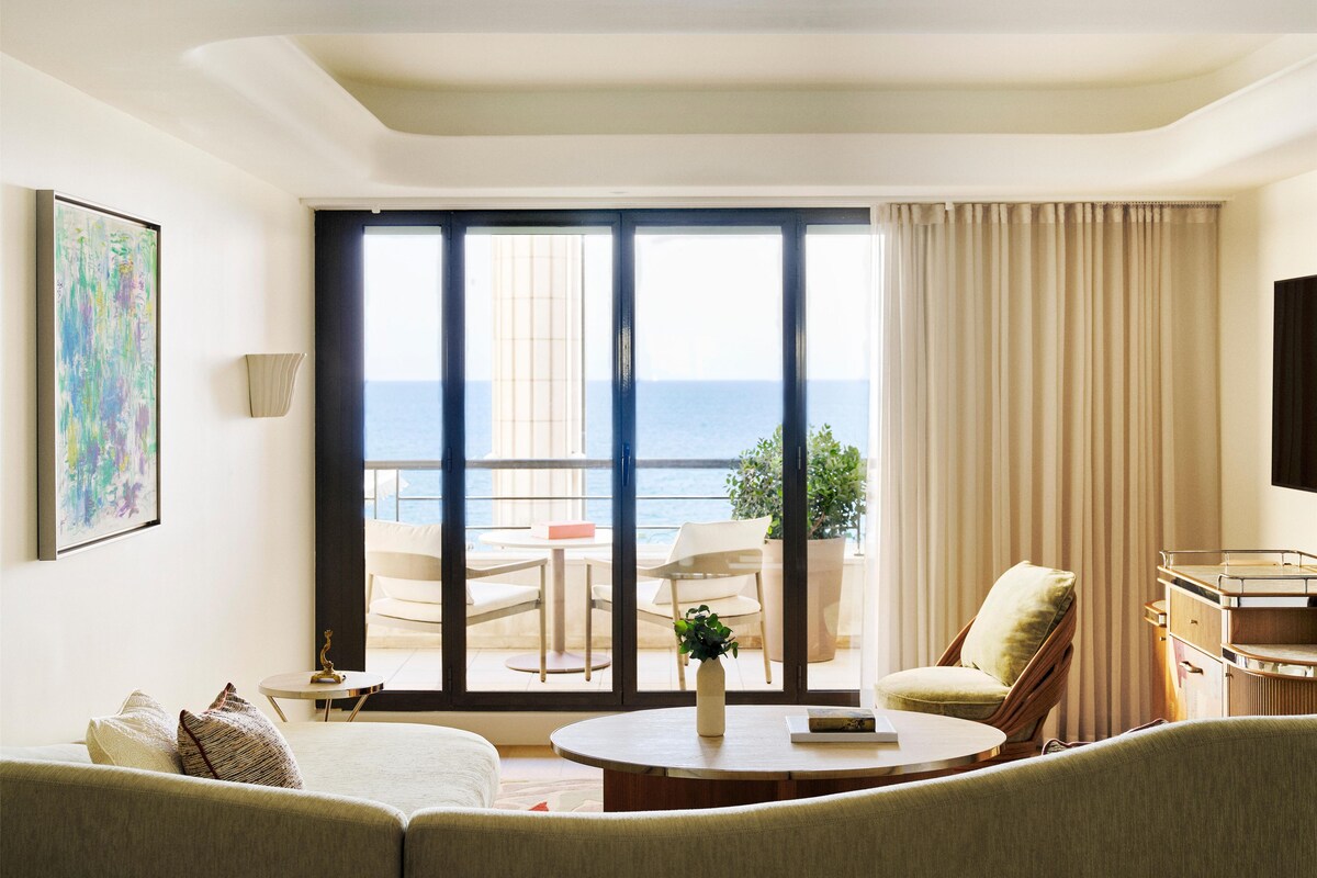 A hotel room with a balcony, a sofa, a round table, and a painting on the wall.