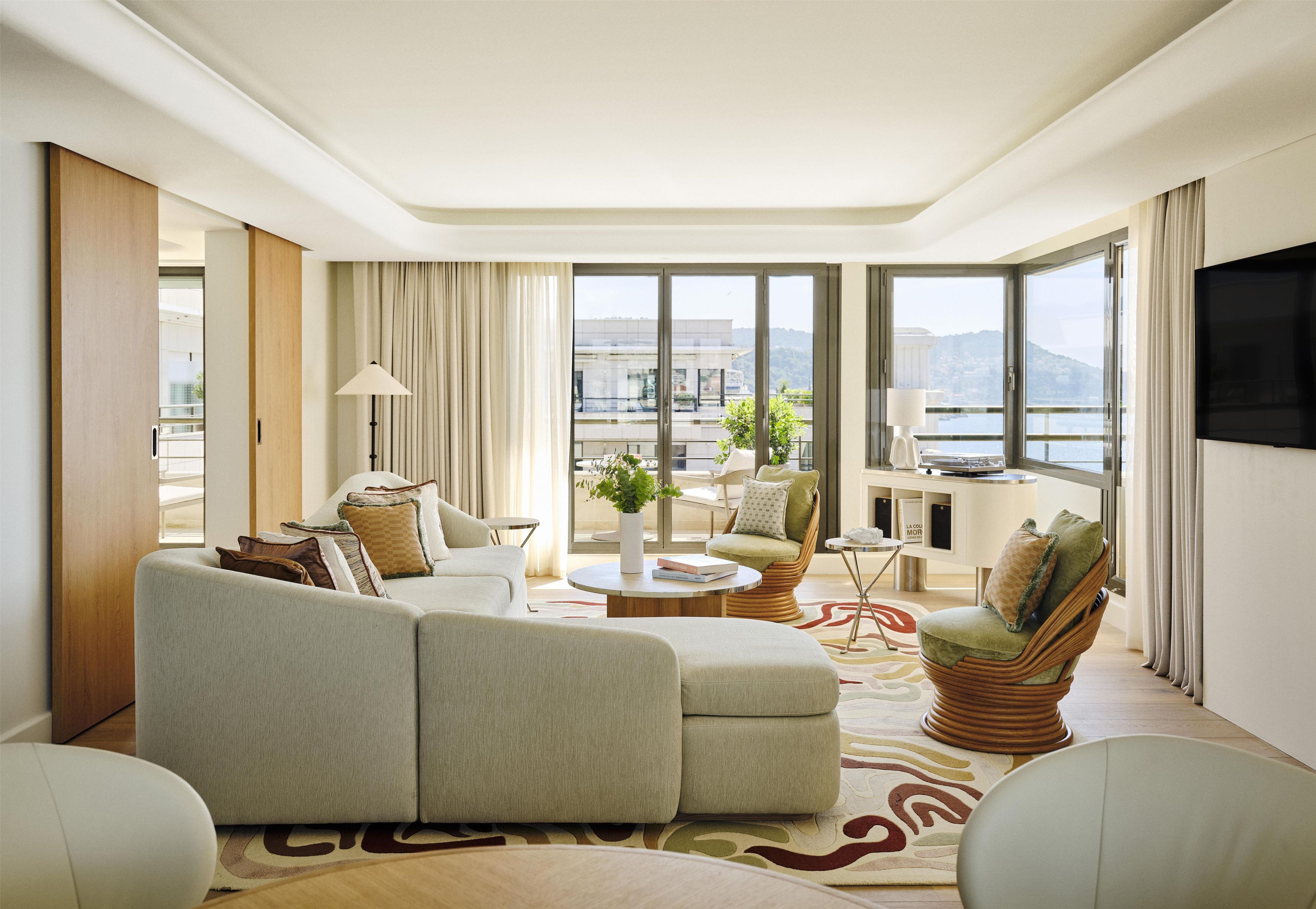 A modern living room with a sofa, armchairs, a coffee table, and a view of the city through large windows.