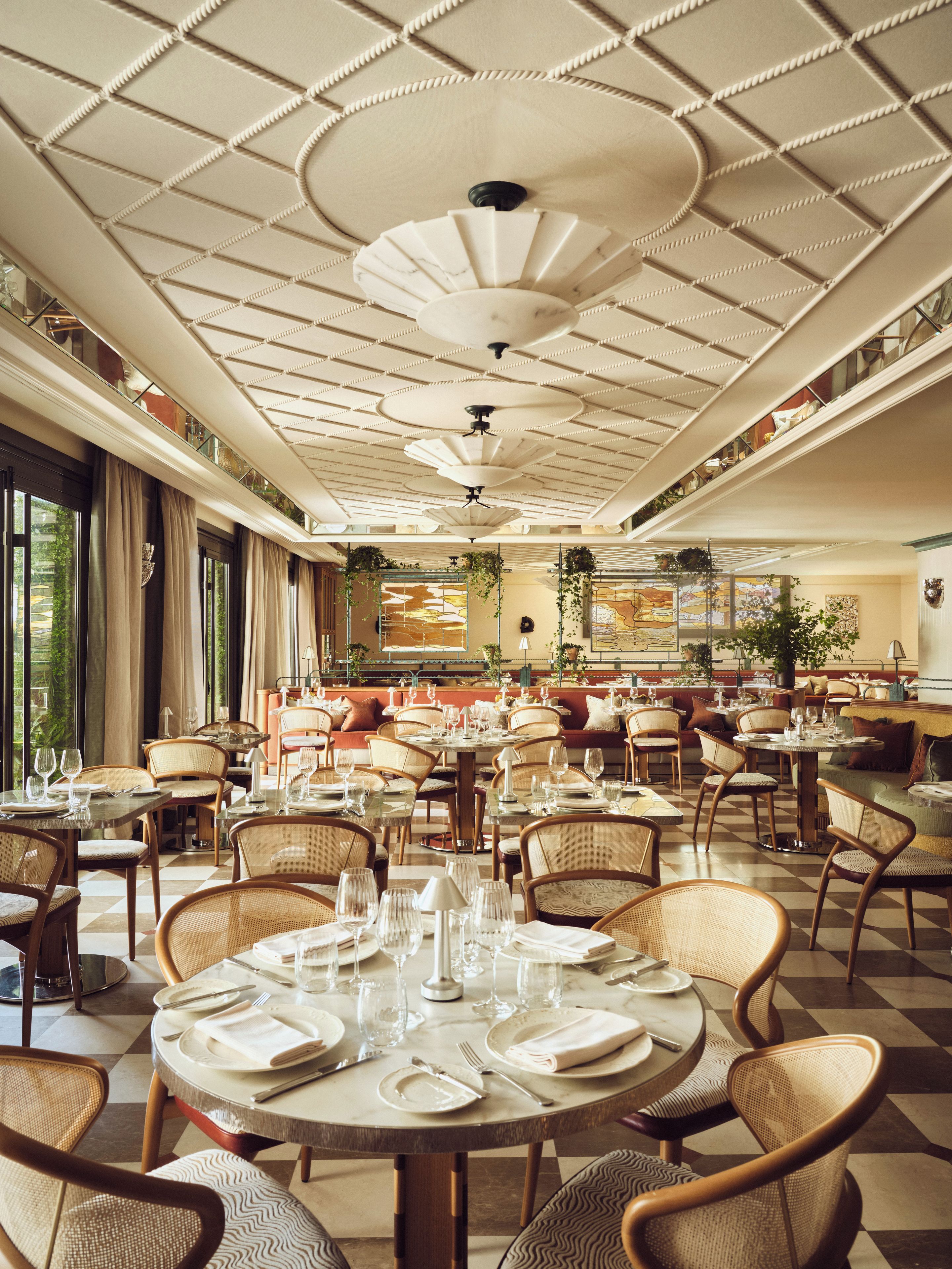 A spacious dining area with multiple round tables set for dining, featuring chairs and a ceiling with a decorative pattern.
