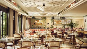 A spacious dining area with multiple round tables set for dining, featuring chairs and a ceiling with a decorative pattern.