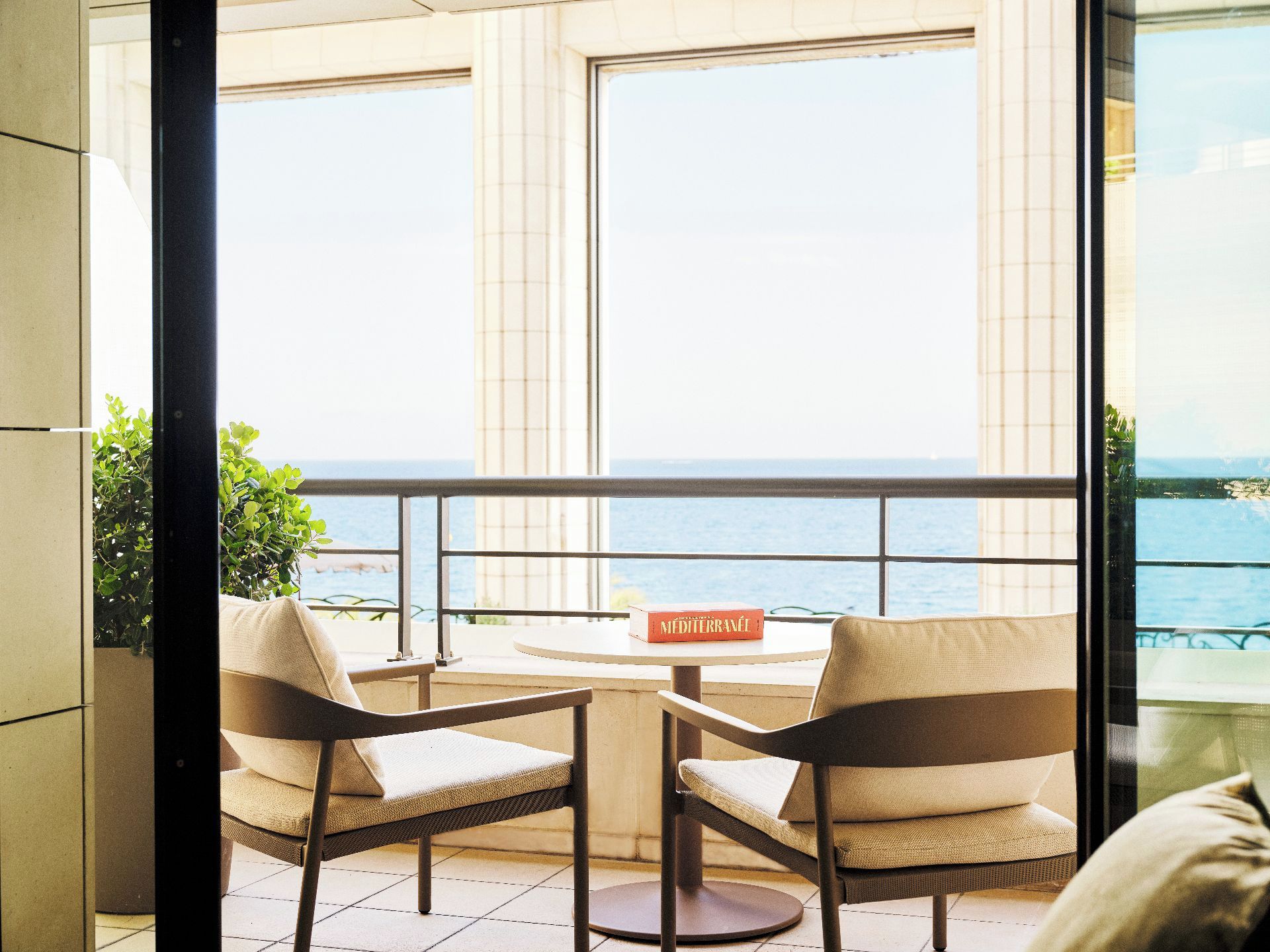 A balcony with a view of the sea, a round table, two chairs, and a book titled 'Méditerranée'.