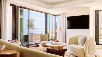 A modern living room with a sofa, armchair, and a coffee table. There is a large window with a view of the sea.