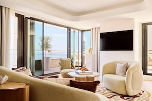 A modern living room with a sofa, armchair, and a coffee table. There is a large window with a view of the sea.