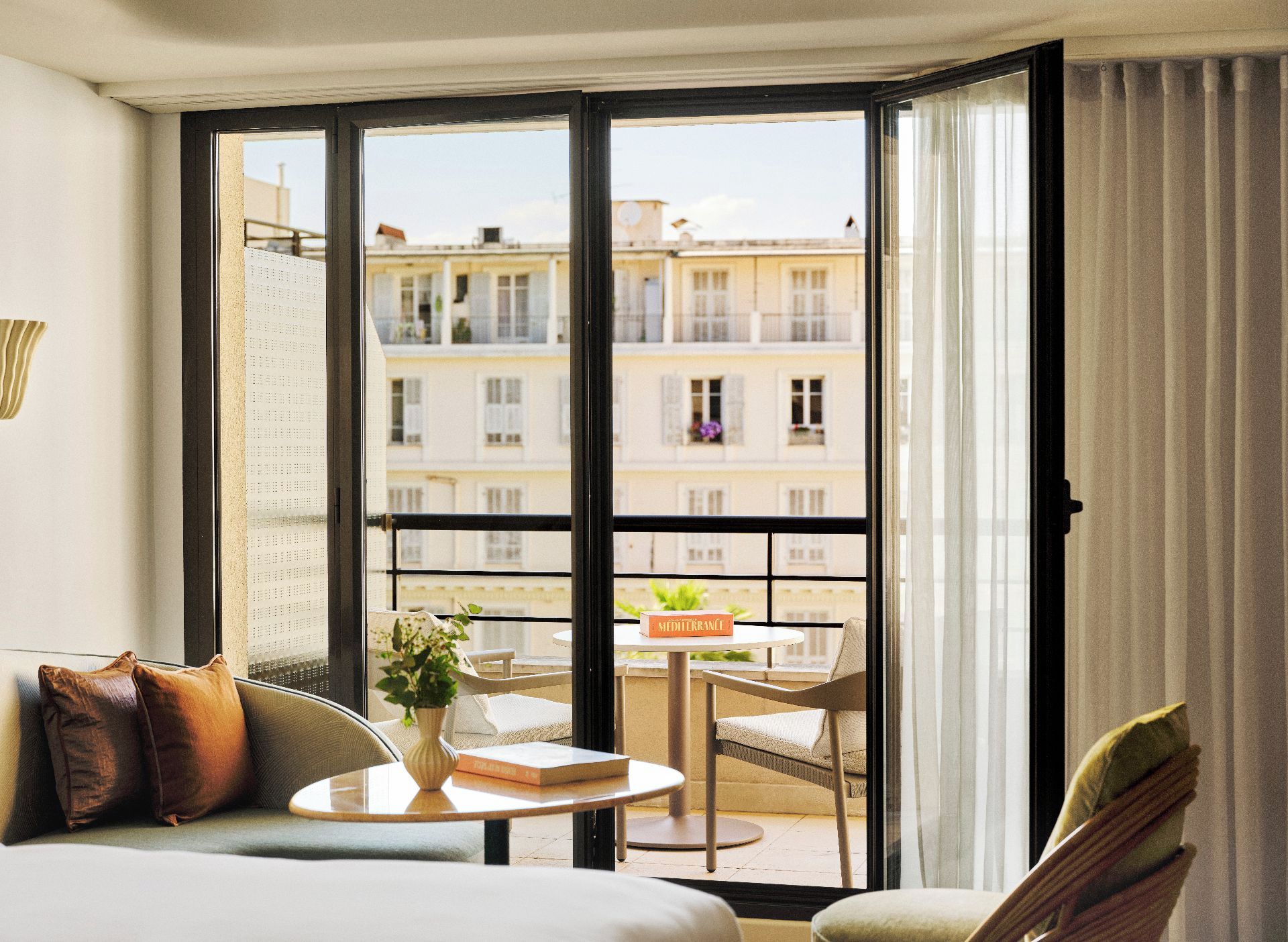 Habitació d'hotel amb balcó, un sofà, una taula petita amb un vas i una cadira.