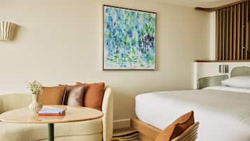 A hotel room with a bed, a round table with a vase and books, a painting on the wall, and a staircase.