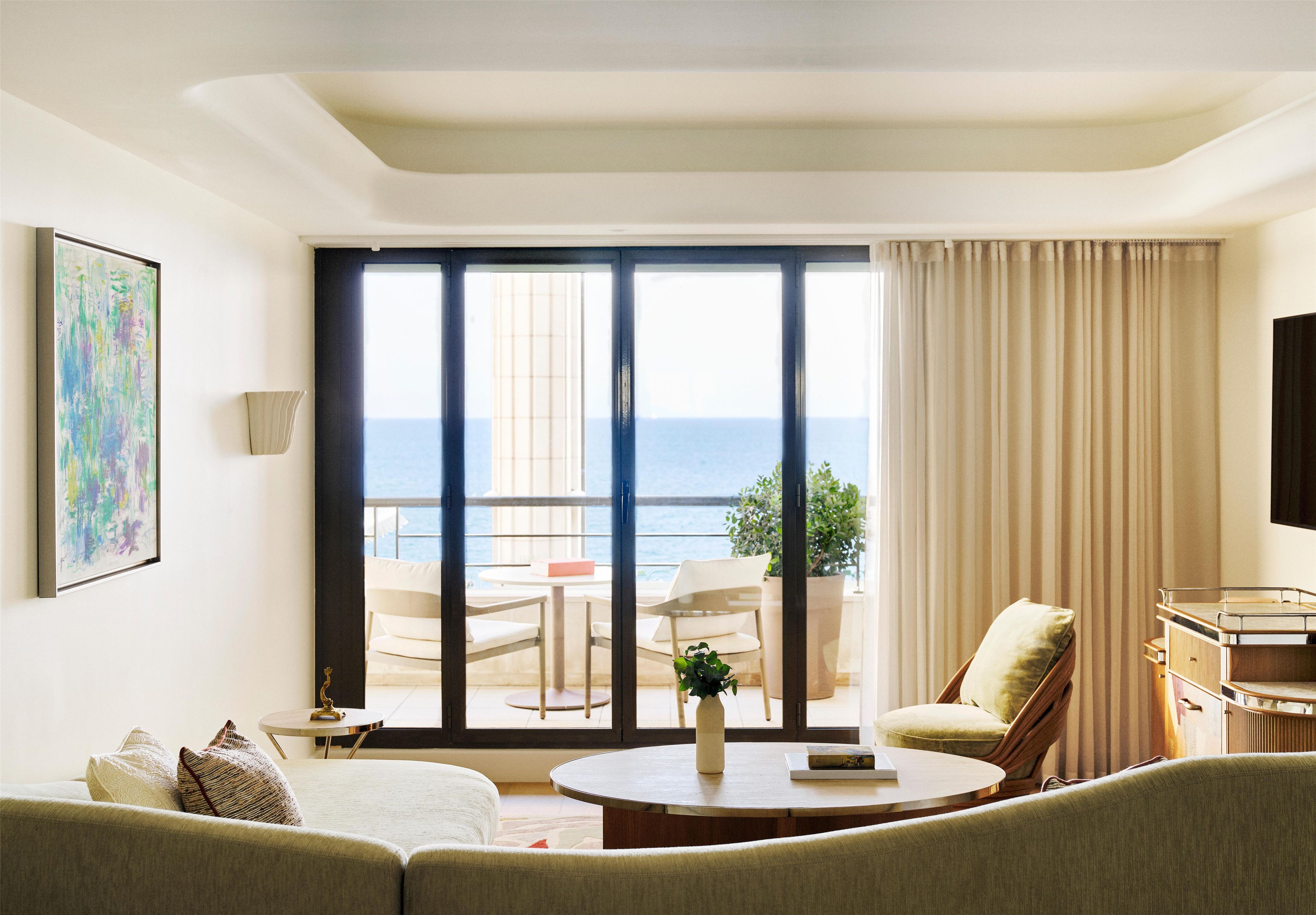 Habitación de hotel con balcón, un sofá, una mesa redonda y un cuadro en la pared.