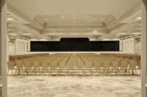 Une salle de conférence avec des rangées de chaises, une scène dotée d’un fond noir et un plafond équipé d’un éclairage encastré.