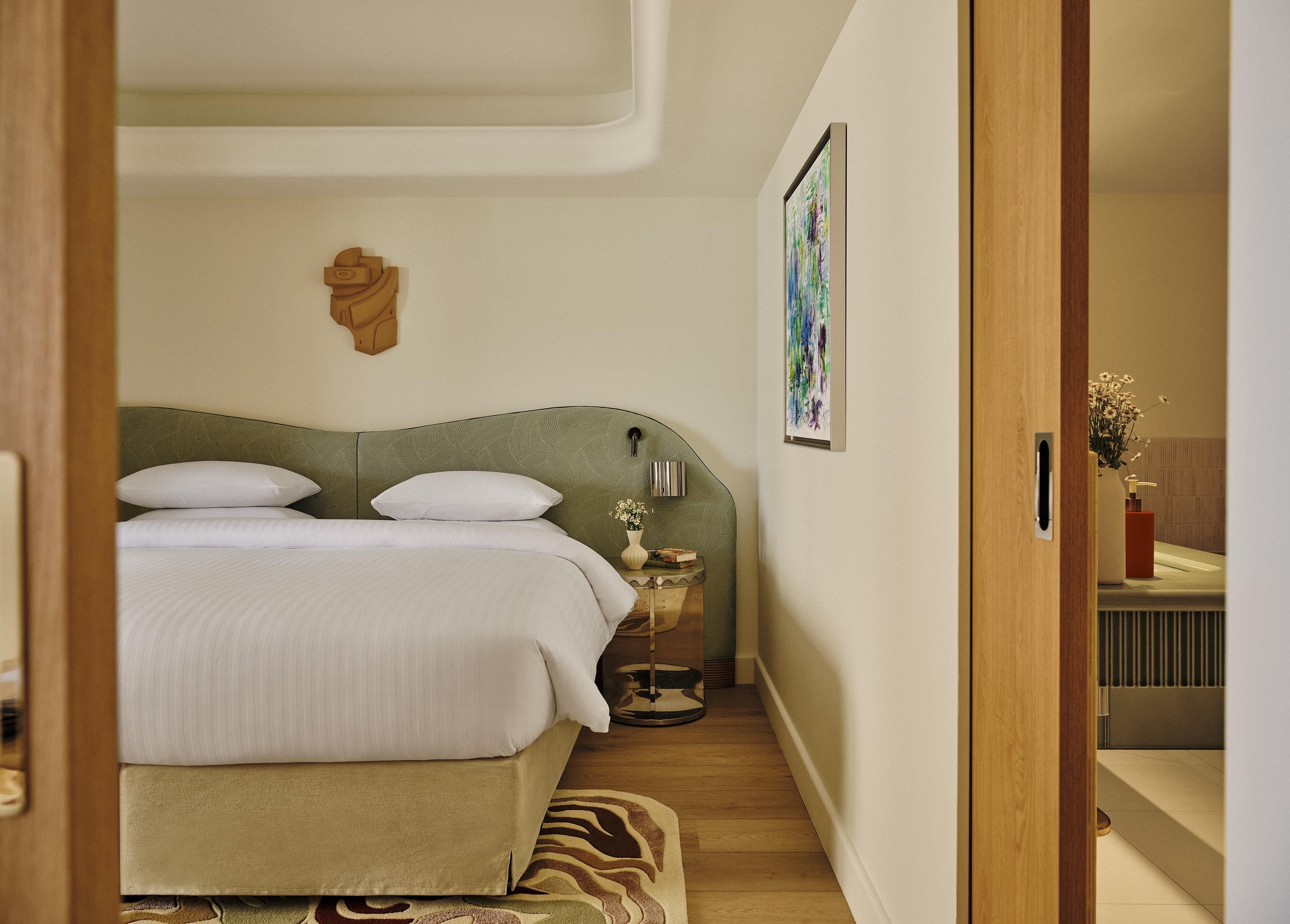 A bedroom with a bed, bedside table, and a painting on the wall.