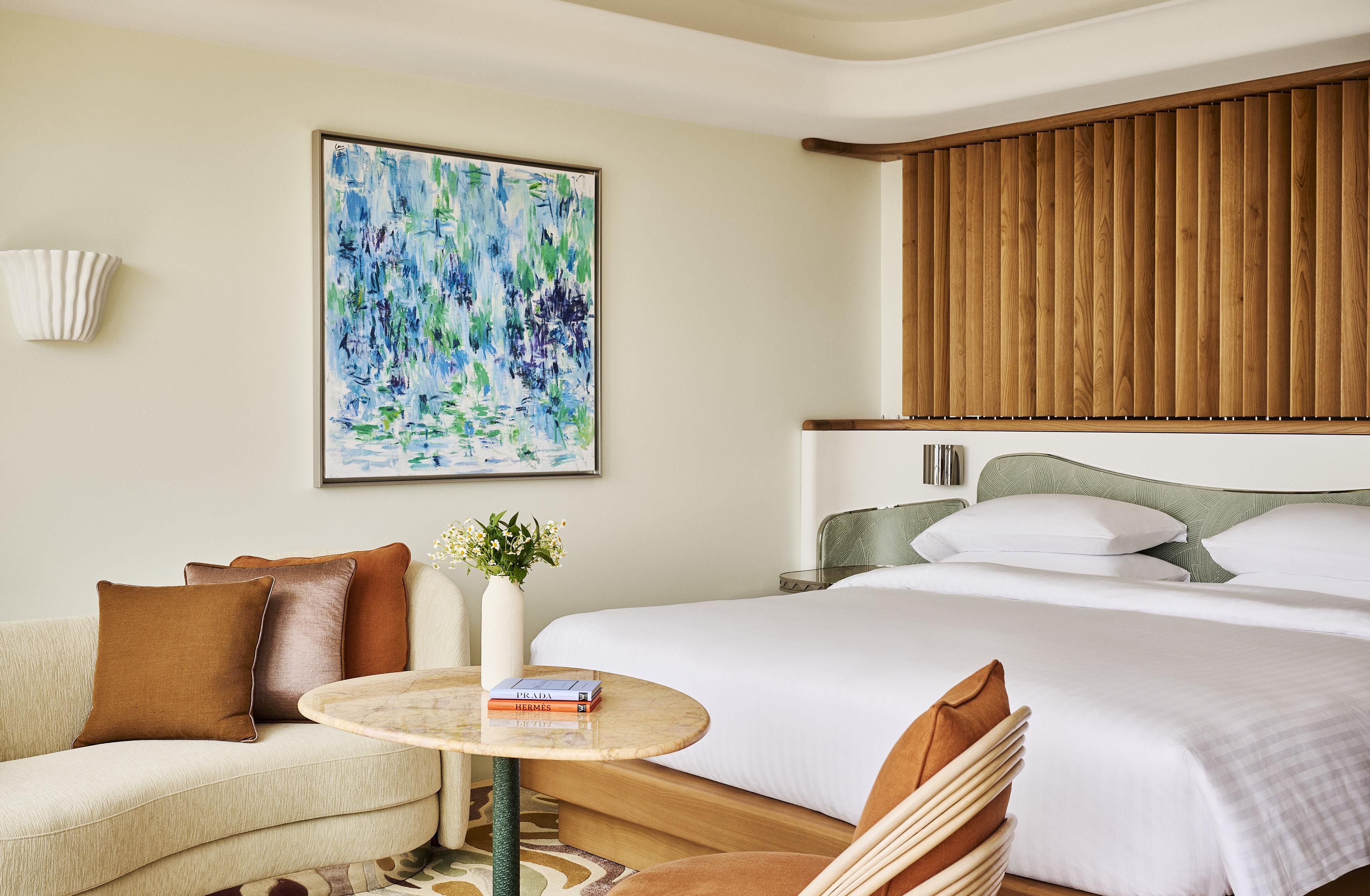 A hotel room with a bed, a sofa, a round table, and a painting on the wall.