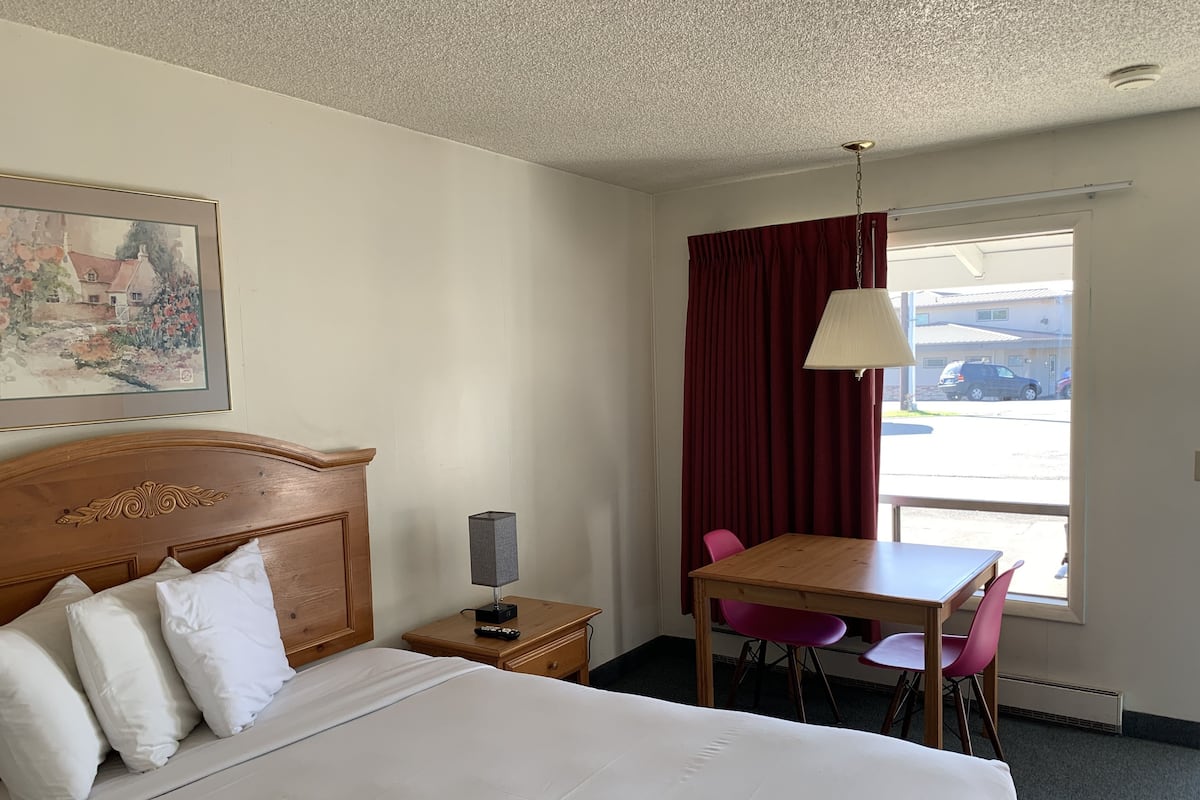 A hotel room with a bed, a desk, a chair, a lamp, and a window with curtains.