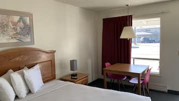 A hotel room with a bed, a desk, a chair, a lamp, and a window with curtains.