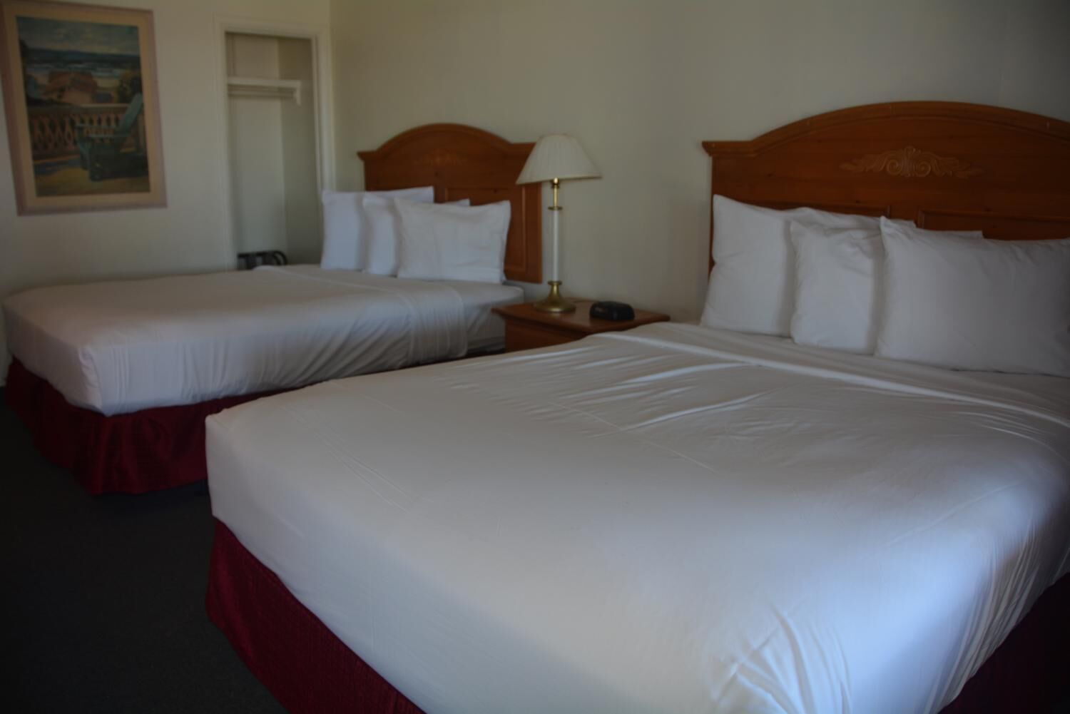 Una habitación de hotel con dos camas, cada una con sábanas blancas y cabeceros de madera. Hay una mesita de noche con una lámpara entre las camas.
