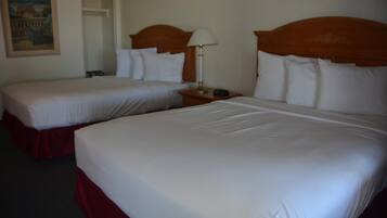 Una habitación de hotel con dos camas, cada una con sábanas blancas y cabeceros de madera. Hay una mesita de noche con una lámpara entre las camas.